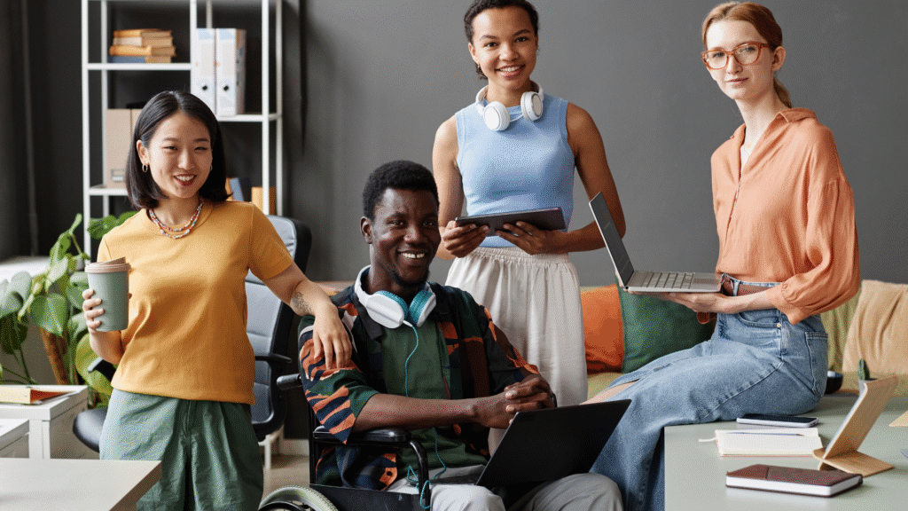Equal Opportunities Diverse group of coworkers smiling in an office, including a Black man in a wheelchair, symbolizing inclusion and accessibility.